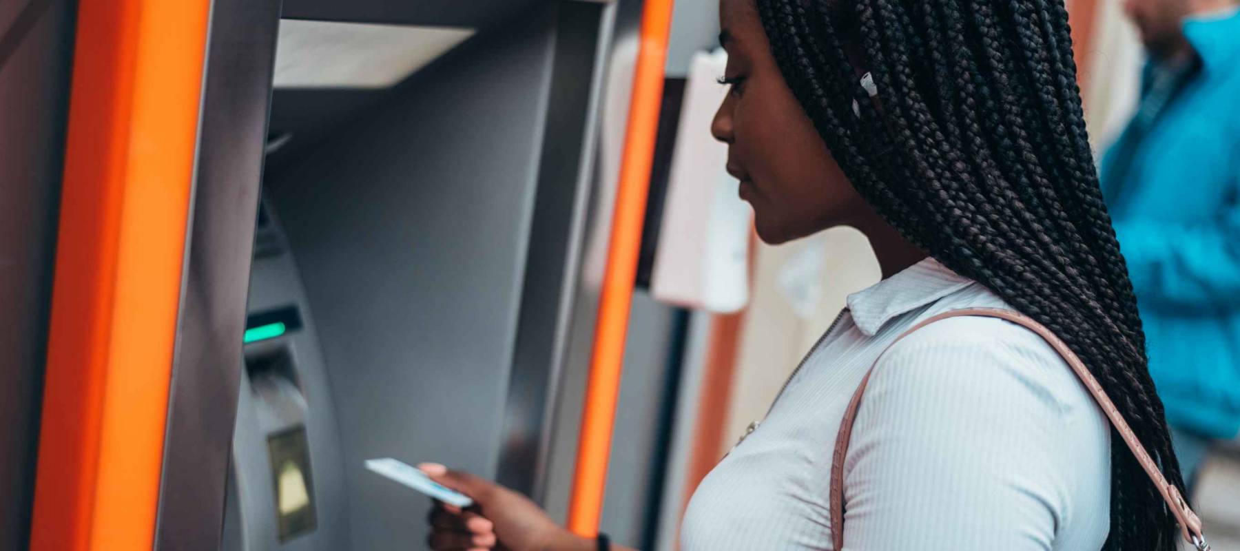 Cheerful african american woman using credit card and withdrawing cash at the ATM