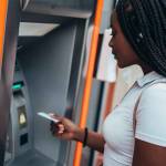 Cheerful african american woman using credit card and withdrawing cash at the ATM