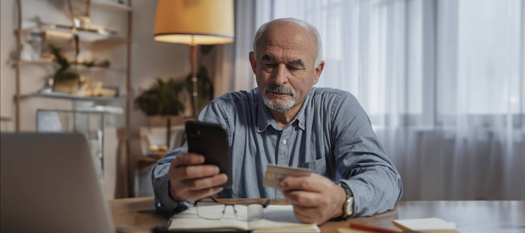 old white man staring solemnly at credit card in one hand and cell phone in the other