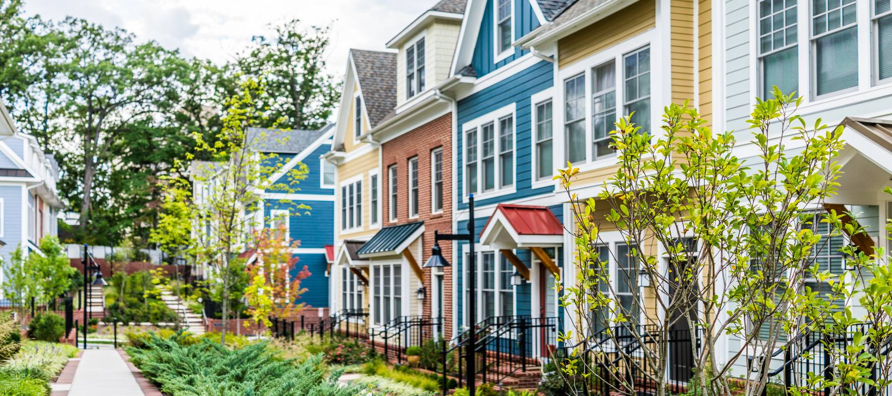 Row of colorful, red, yellow, blue, white, green painted residential townhouses, homes, houses with brick patio gardens in summer
