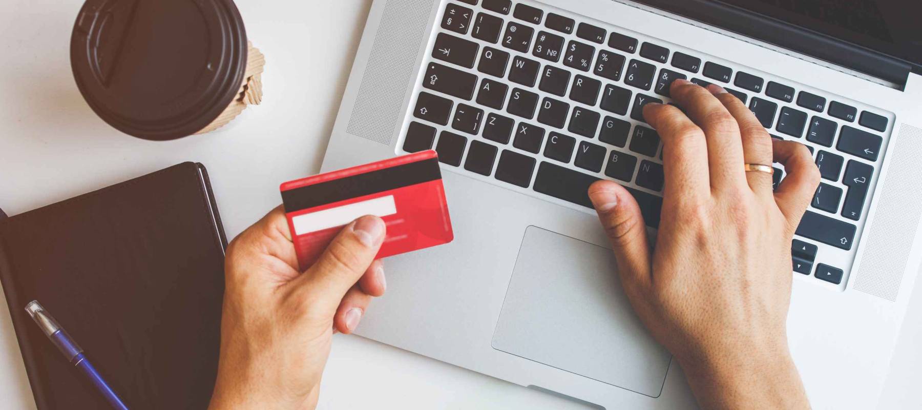 a white man's hand typing on a laptop and holding a credit card