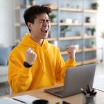 happy man joyful by laptop fists clenched celebrating