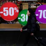 Woman walks by a big store front with sales advertisements.