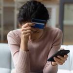 Upset female with head and credit card in one hand and phone in the other sitting on couch