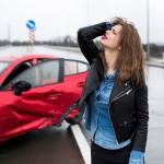 An upset young woman stands in front of a car that's been in a car accident