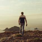 Travel photographer walking towards the cliff to take a panoramic landscape photo at sunset.