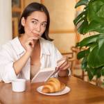 Smiling beautiful girl with a book, reading with thoughtful smirk, thinking of something, drinking coffee in cafe.