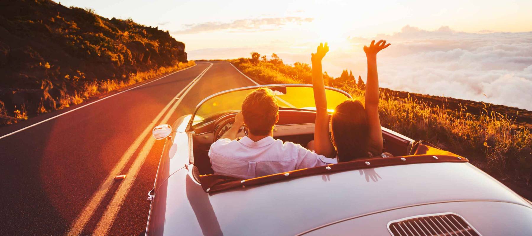 Happy Couple Driving on Country Road into the Sunset in Classic Vintage Sports Car