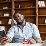 man looking disappointed at his phone while holding a credit card