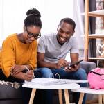 Young African Couple Sitting On Sofa Calculating Invoice