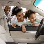 Cheerful Black Family Of Three Buying New Car, Looking Through Window At Auto Interior Choosing Luxury Automobile In Dealership. Vehicle Rent And Purchase Concept