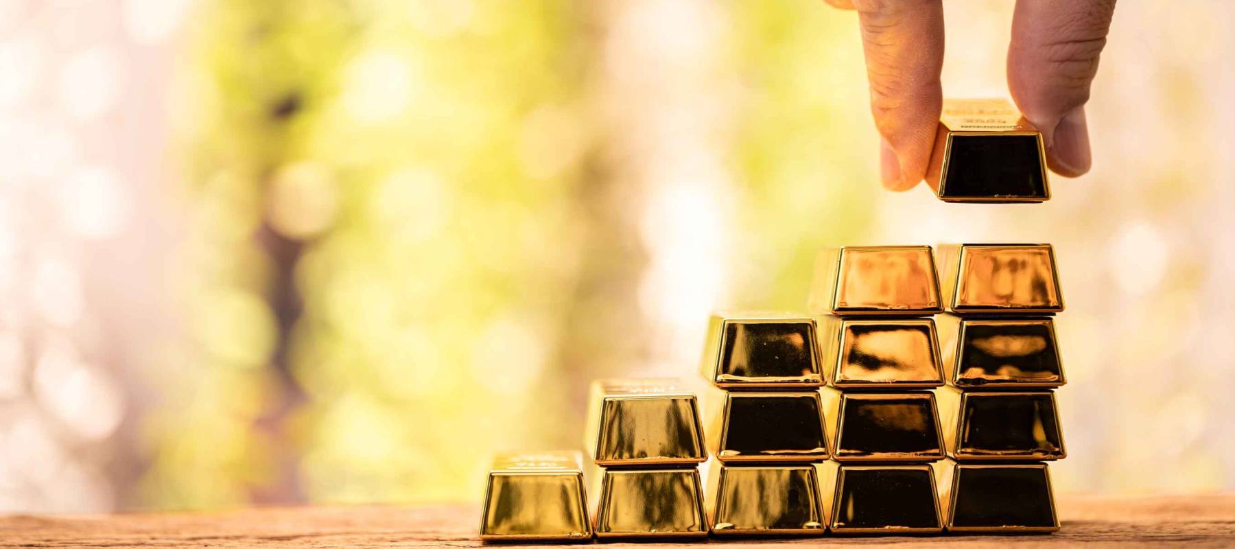 Man hand hold the gold bar with high value for invest and stack picked up put on the old wood on the morning sunlight in public park, Targeting of business to winner and success concept.