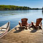 Two Adirondack chairs on a wooden dock facing the blue water