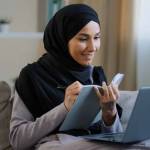 Cheerful young muslim arabian lady young woman on couch with laptop