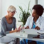 A female doctor sits at her desk and chats to an elderly female patient while looking at her  test results