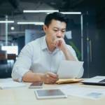 Stressed young asian businessman working from office report annoyed with low sales. Nervous boss see c mistake incorrect information in paper document