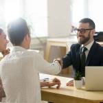 Smiling lawyer, realtor or financial advisor handshaking young couple thanking for advice,