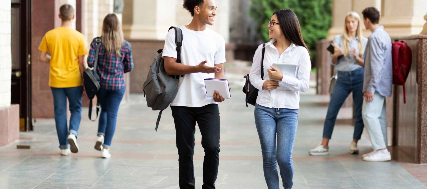 Diverse classmates chatting, walking after classes in university campus outdoors