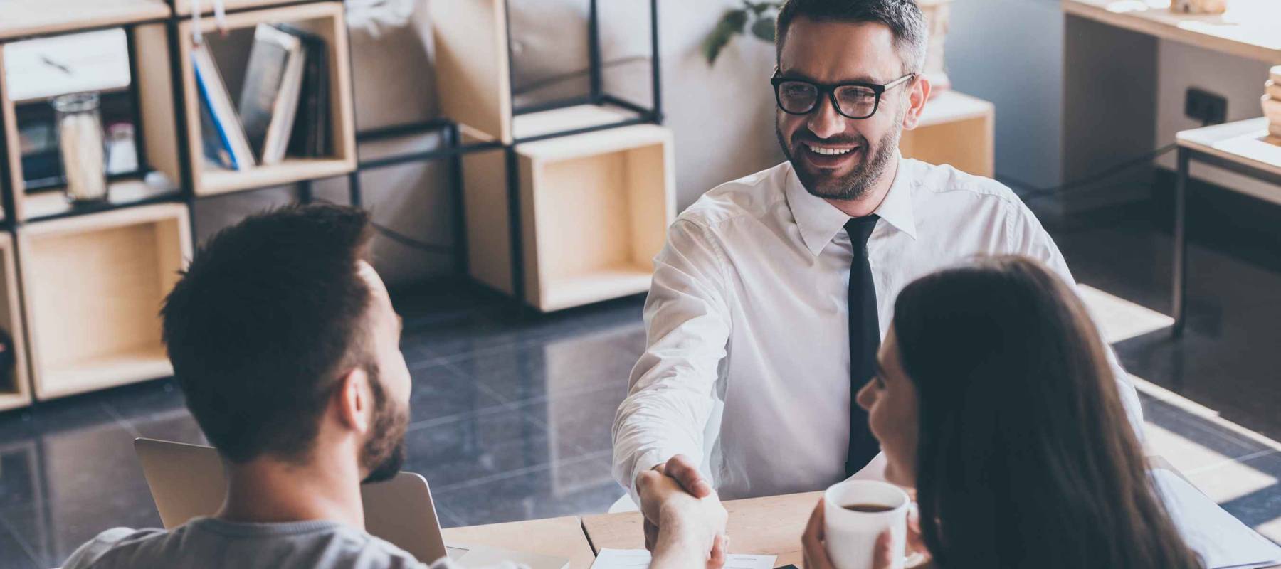 Sealing a deal. Top view of two men sitting at the desk and shaking hands while young woman looking at them and smiling