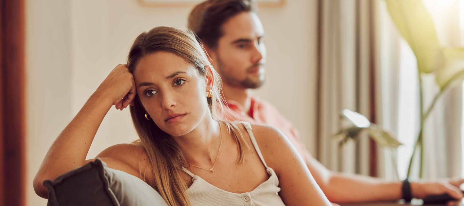 Unhappy, sad and annoyed couple after a fight and are angry at each other while sitting on a couch at home. A woman is stressed, upset and frustrated by her boyfriend after an argument