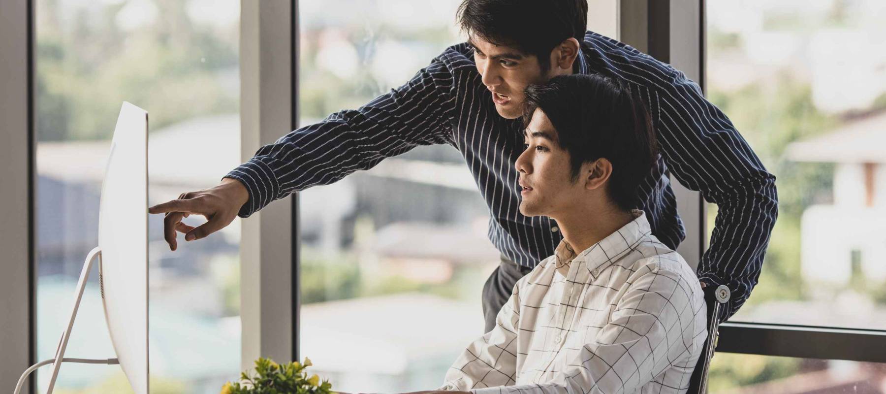 teen older brother stand pointing computer monitor explaining when help teaching younger one sitting learning to invest online