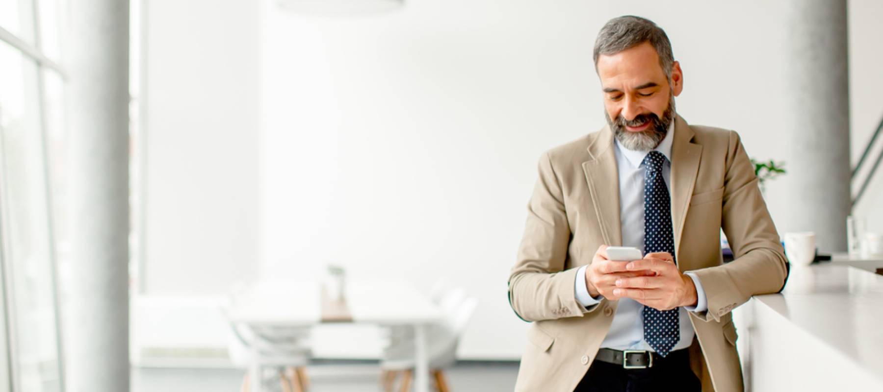 an older man in a suit and office environment, looking at phone