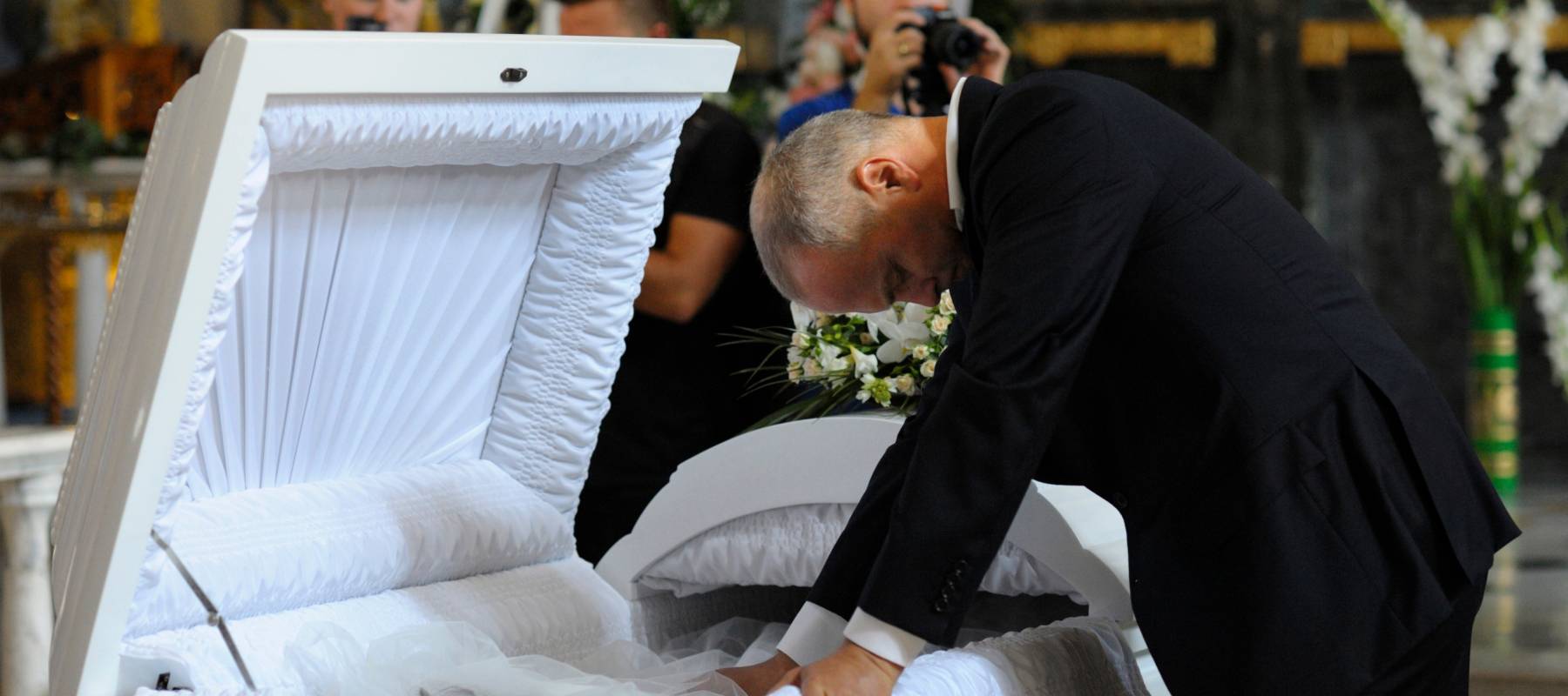 Man stands mourning over a white casket