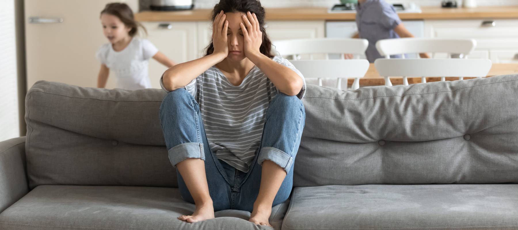 Tired and frustrated mum sits on a couch as kids run around