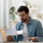 Young man reviews banking paperwork at the kitchen table
