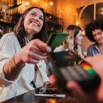 Happy young woman tapping credit card at a restaurant