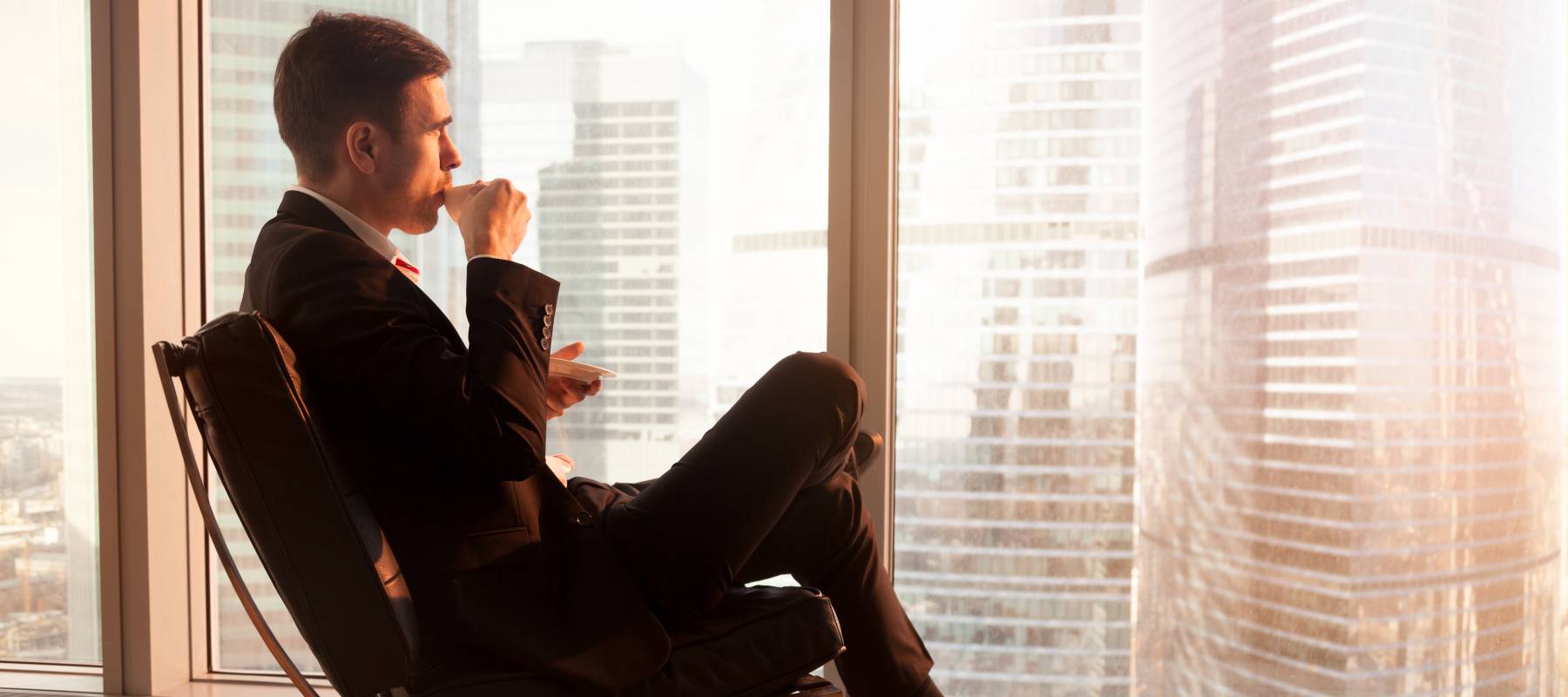 Man sips coffee looking out of the window of his luxury apartment