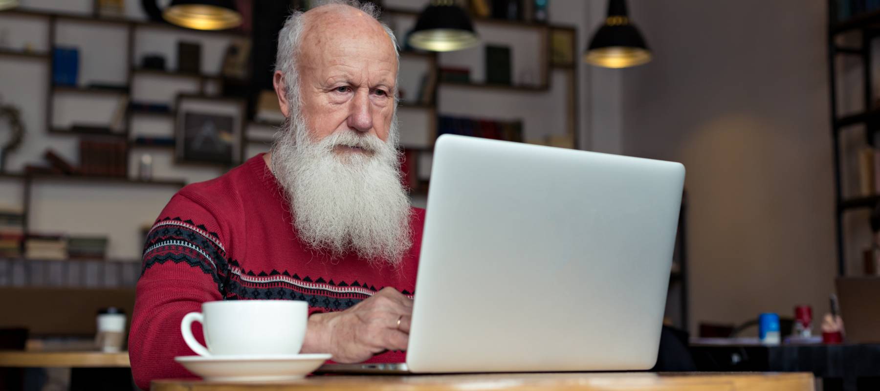 Older, retired man sitting in a cafe checking his laptop
