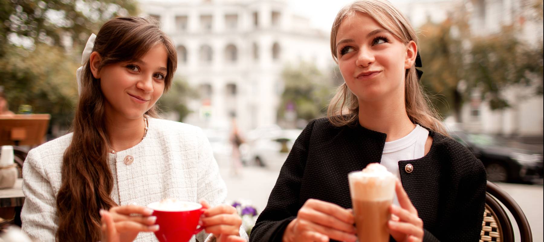 Two young adults giggle over lattes at an outdoor cafe