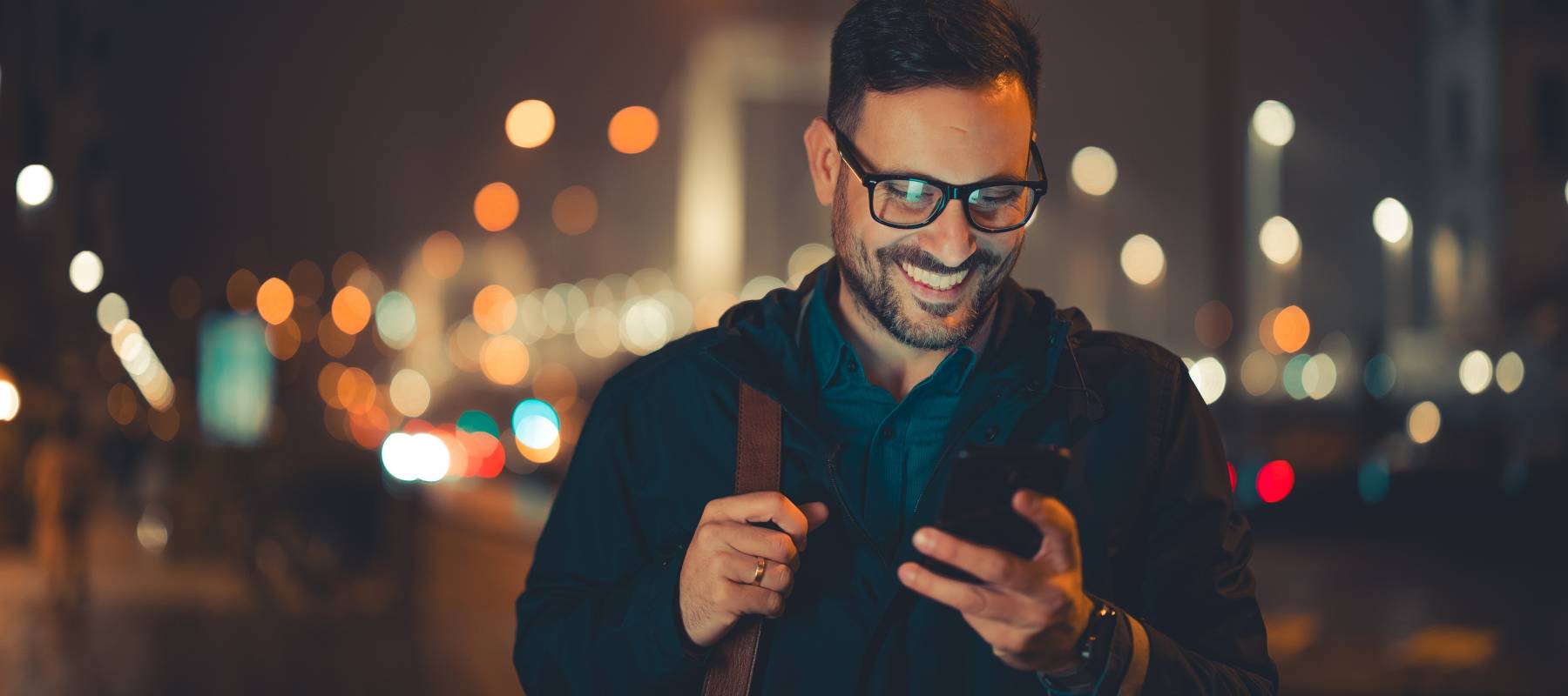 Man smiling at phone with city lights behind him