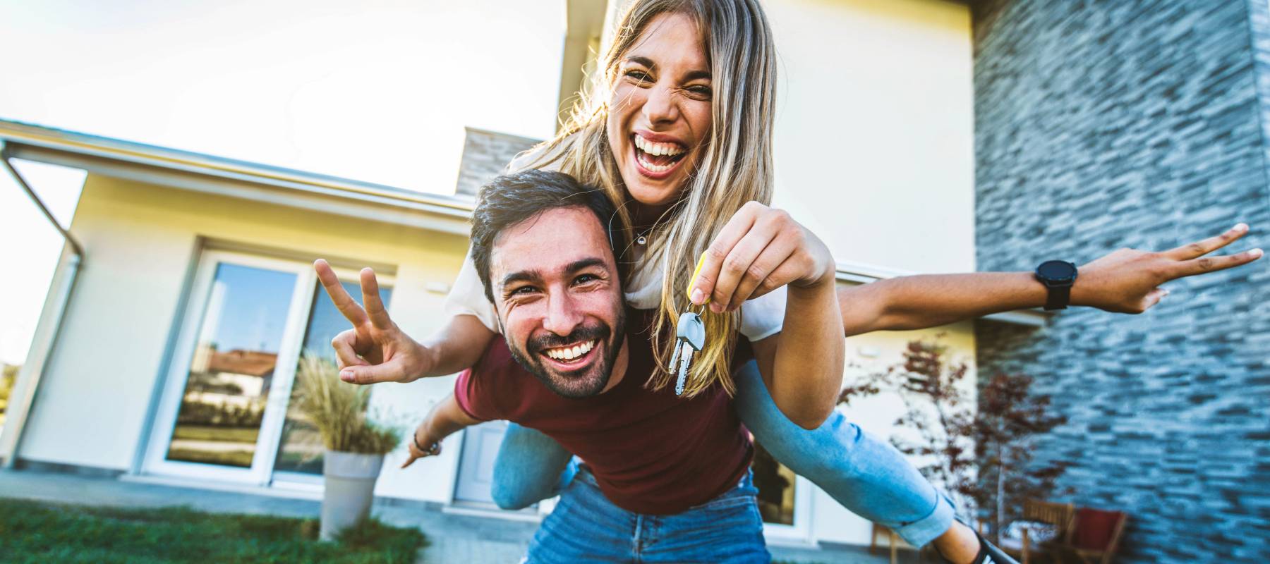 Happy young couple posing with keys in front of new home