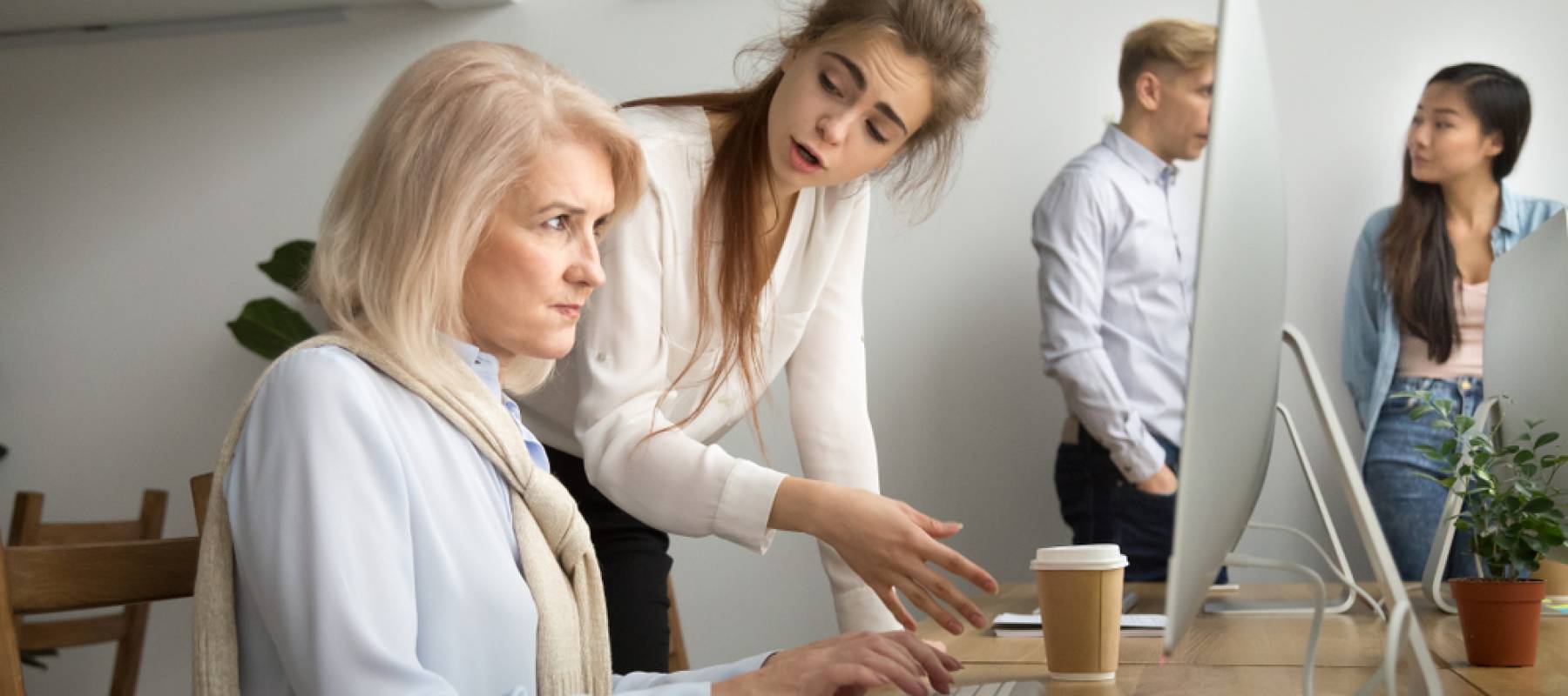 Young team leader correcting offended senior employee working on computer in office