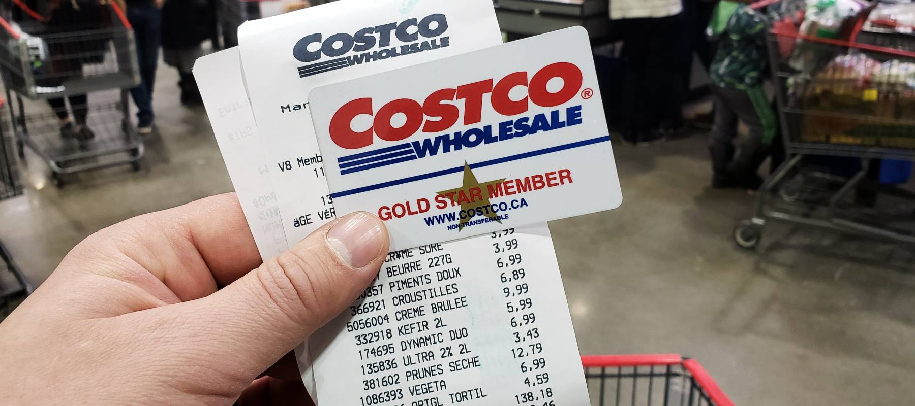 Hand holding Costco member card and receipt in front of shopping cart