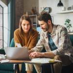 Couple Using Laptop Computer, Sitting on Sofa in Apartment.