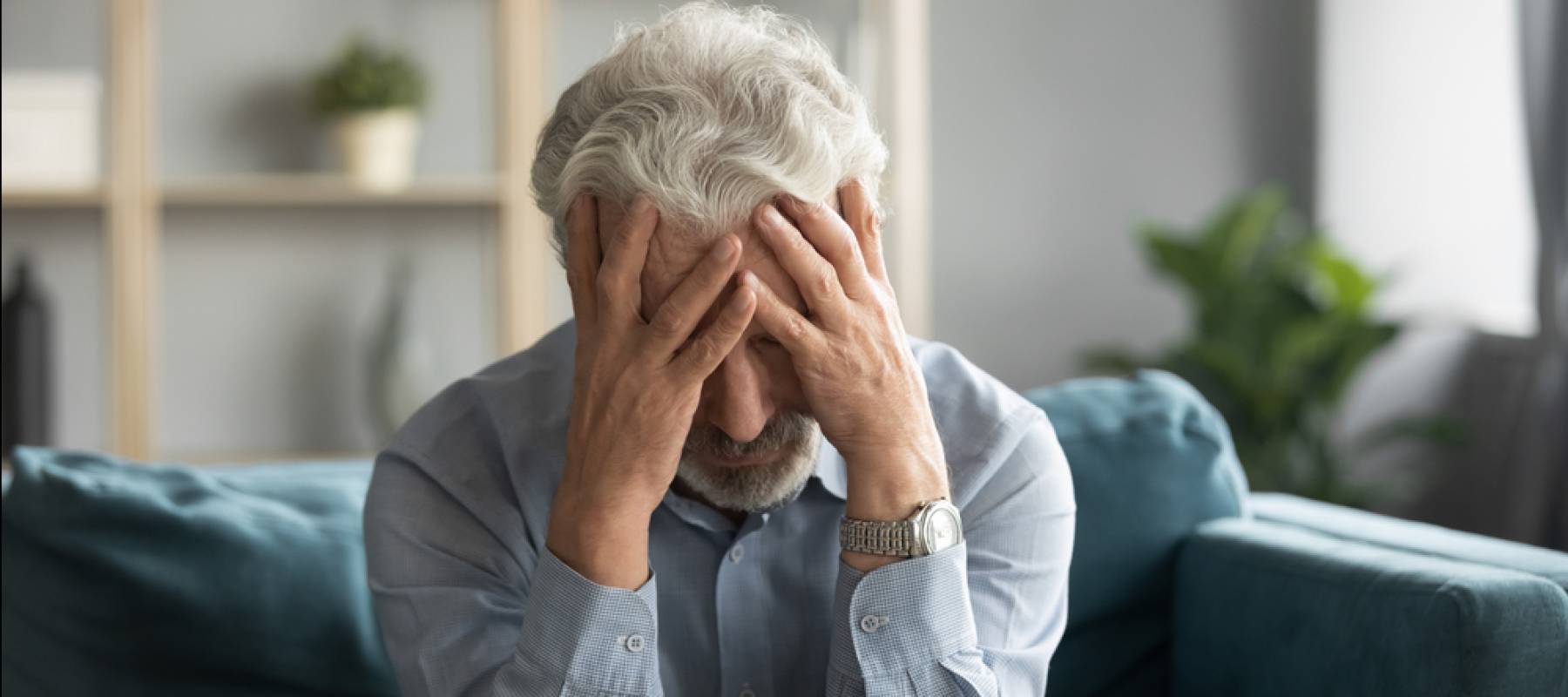 Depressed old 60s man sit on couch in living room