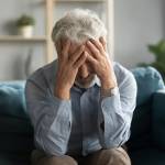 Depressed old 60s man sit on couch in living room