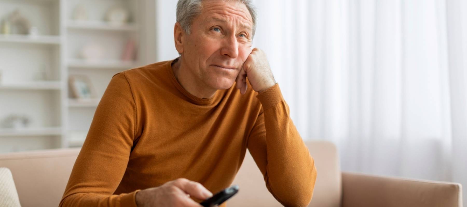 Unhappy senior man with remote control in his hand sitting on couch at home