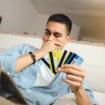Man holding four credit cards looking at his computer