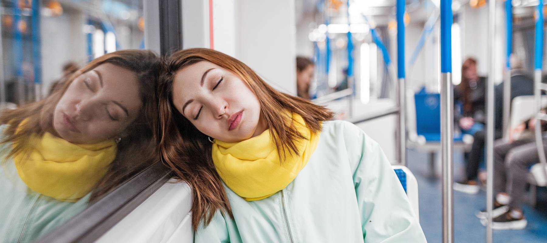 A brightly-dressed Gen Z female riding the subway asleep, and resting her head against the window.