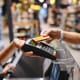Cropped close up woman hand arm shopping at supermarket put credit card to wireless modern bank payment terminal process acquire payments near cashier checkout inside store. People purchasing concept