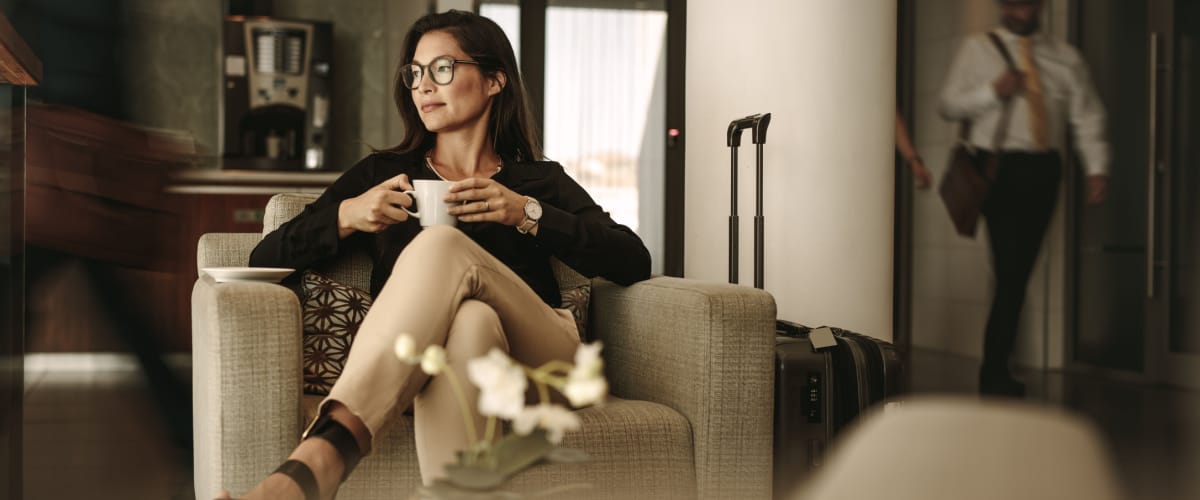 woman sits in lounge chair drinking a coffee in the airport lounge