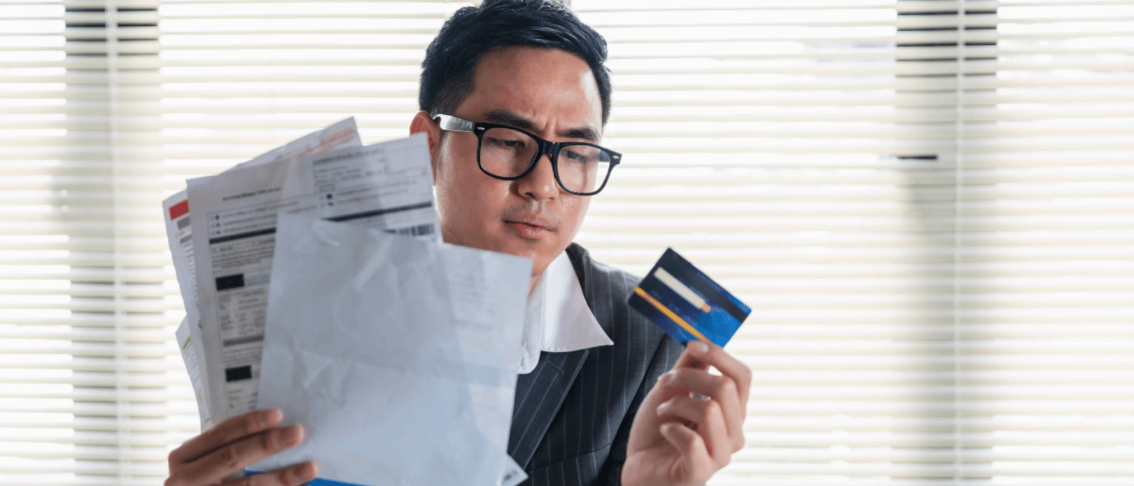 Stressed young asian businessman holding so many expenses bills electricity bill,water bill,internet bill,cell phone bill and credit card bill in his hand no money to pay debt