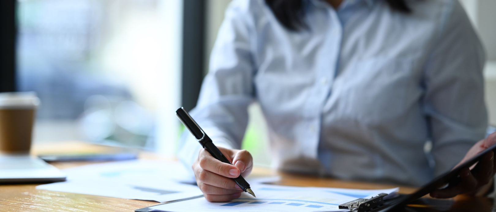 Cropped shot of female economist working with sales statistics document at office desk