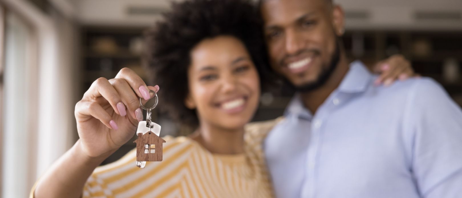 Happy Black millennial couple showing keys, smiling at camera, hugging. 