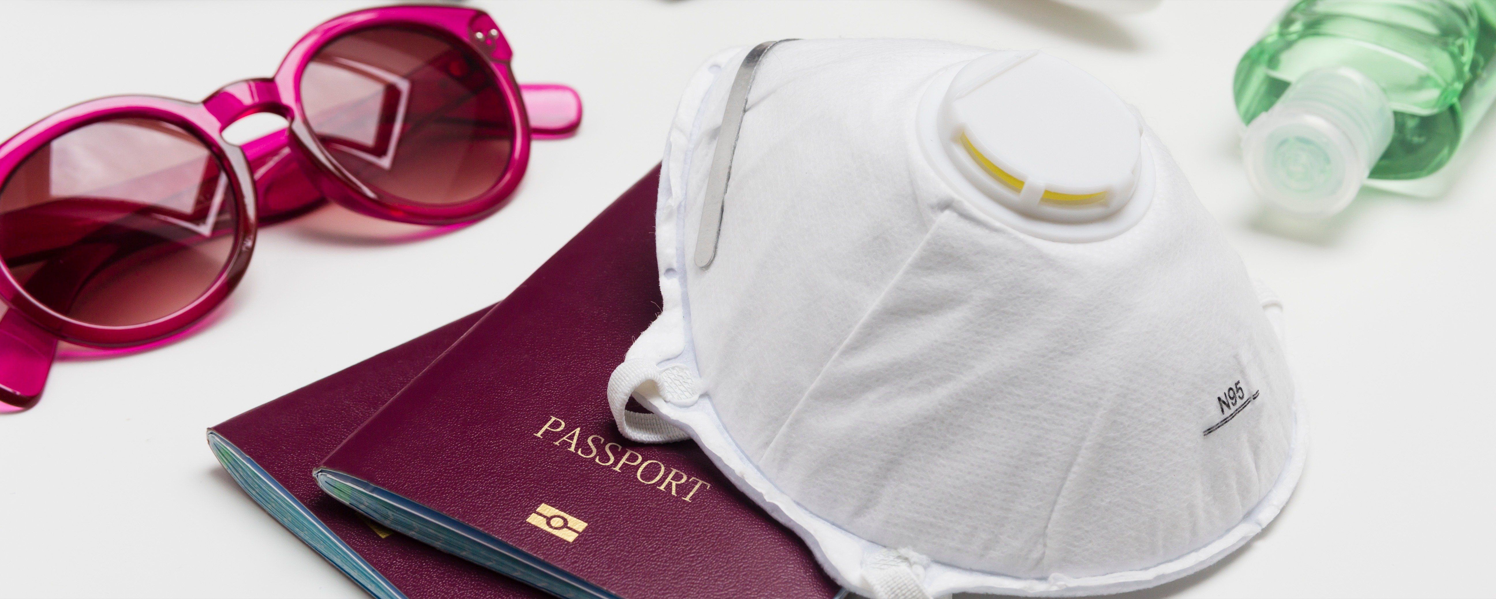 Travelling during the coronavirus outbreak. Passport with face mask, sunglasses and hand sanitizer gel.