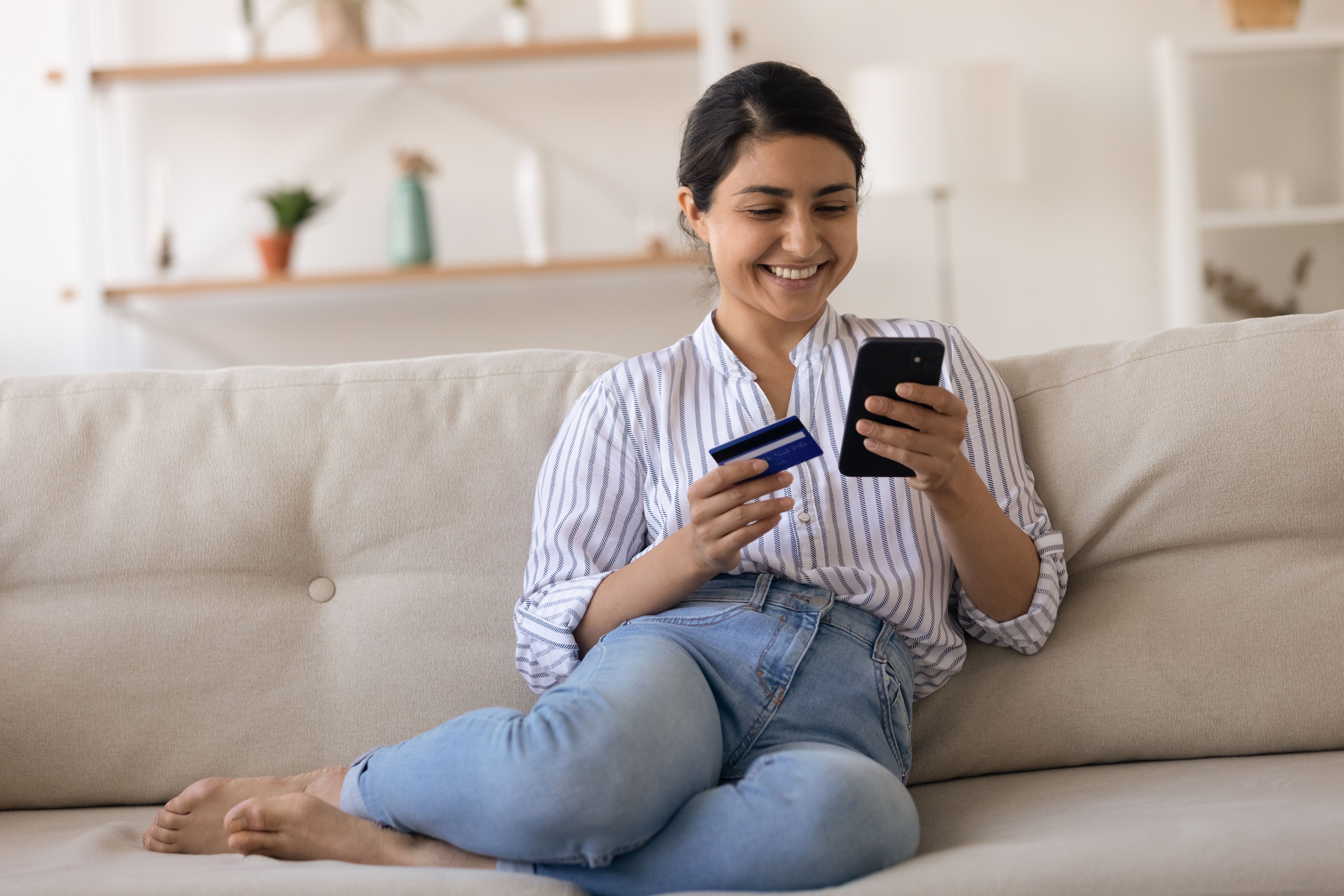 Woman smiling at her phone as she looks at her bank account. She's holding her bank card in her other hand.